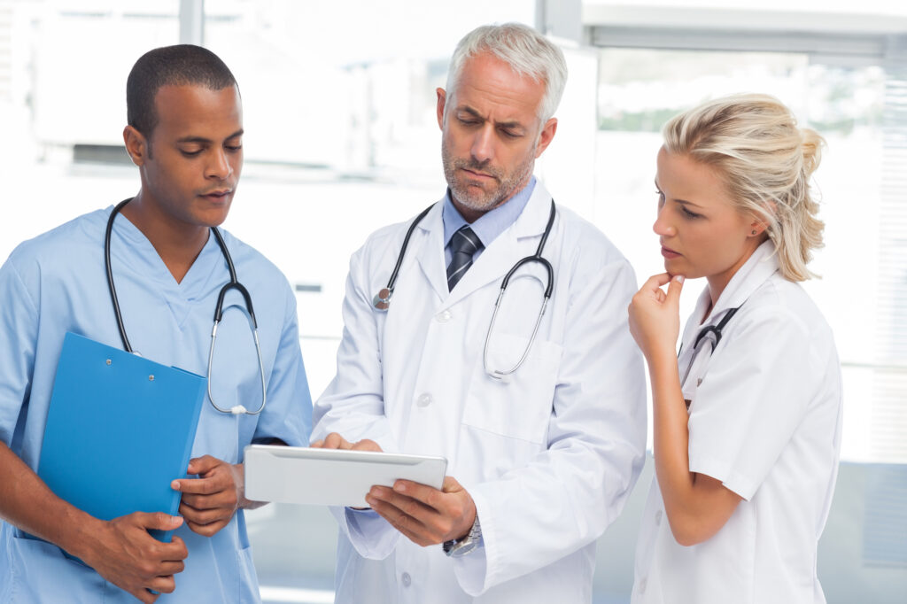 male physician with a male nurse on one side and a female nurse on the other side reviewing a patient chart