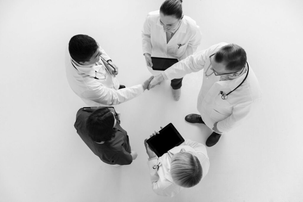 black and white aerial view of five clinicians with two doctors shaking hands