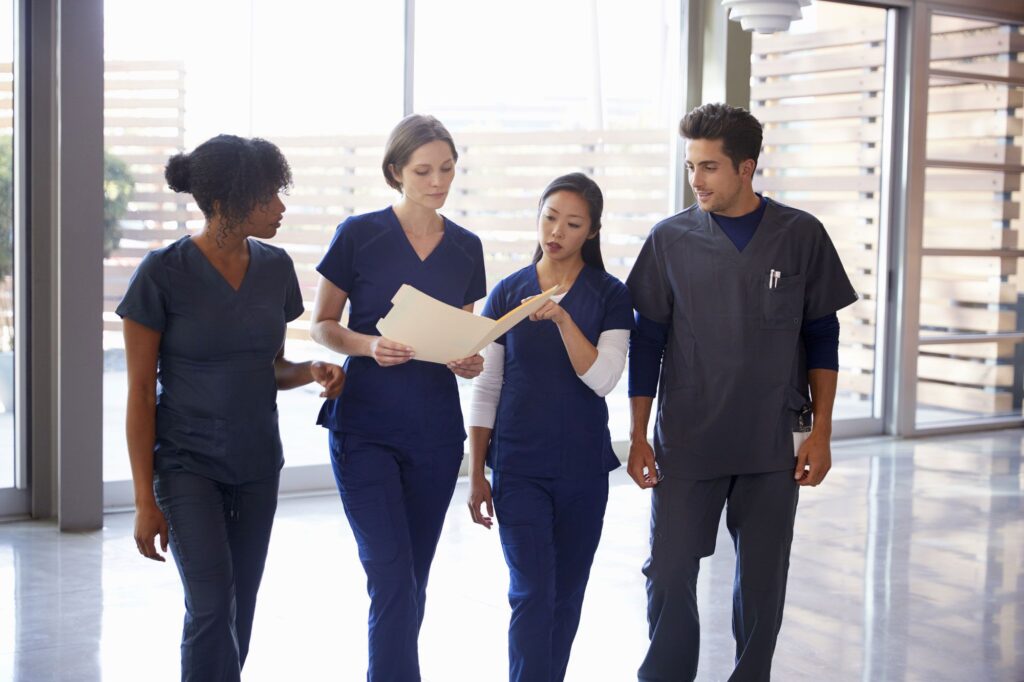 diverse group of young clinicians in blue scrubs looking at a document inside a folder