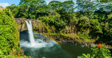 photo of Rainbow Falls in Hilo, Hawaii, with a rainbow over a waterfall with lush trees and greenery around the waterfall