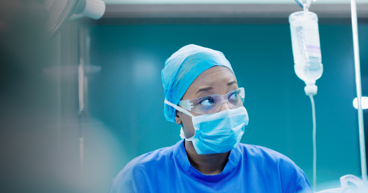 CRNA nurse in operating room wearing blue scrubs, a face covering, and protective eyewear